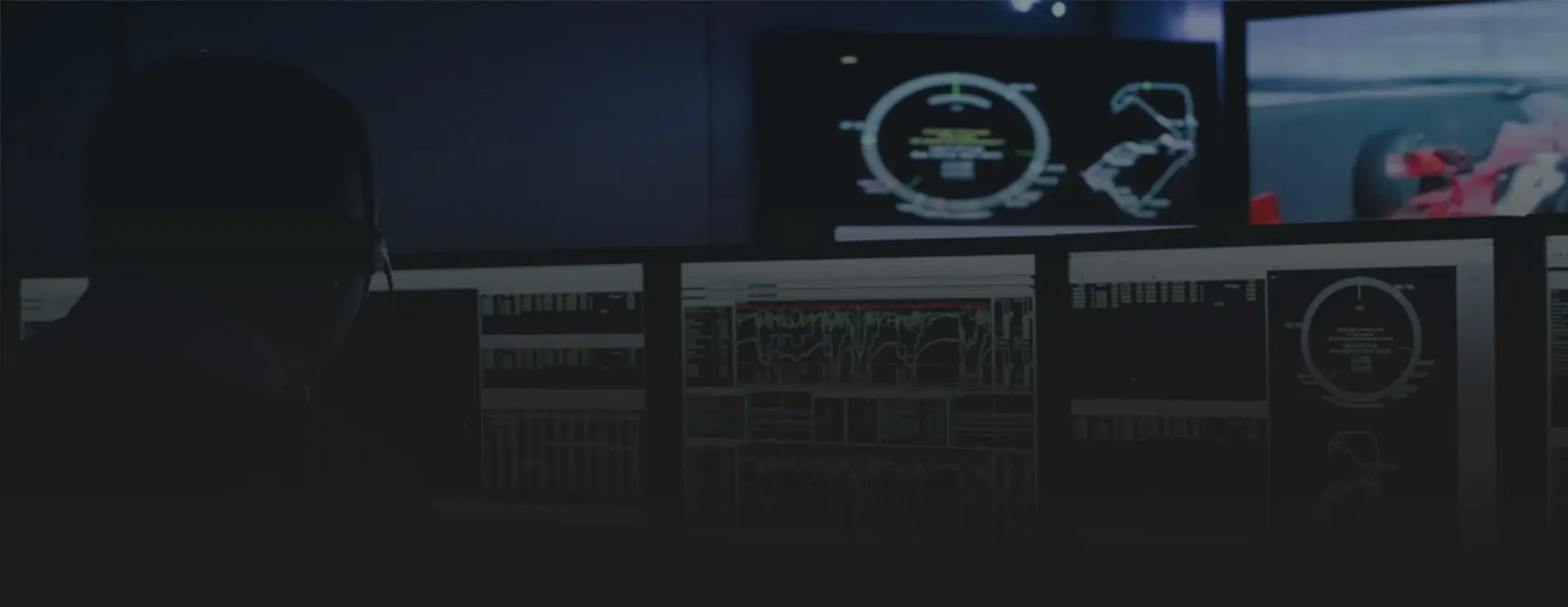 A race engineer uses ATLAS in a race team strategy room. Multiple screens show race telemetry and other information, and another screen shows a red race car is shown on track.