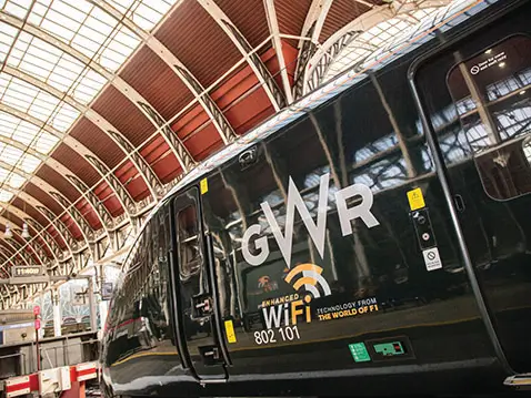 Dark green GWR train at a covered station platform, with large “GWR” lettering and “WiFi 802 101” branding visible on the side under an arched glass roof.