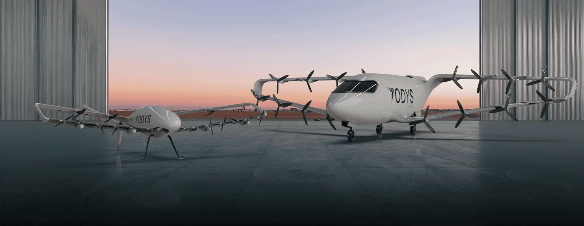 Two white electric aircraft with multiple rotors, branded ‘ODYS,’ positioned inside a hangar at sunset, with one larger aircraft and a smaller companion vehicle shown side by side.