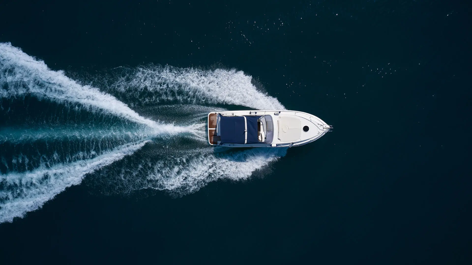 Overhead view of a motorboat moving through dark blue water, leaving a white wake behind.